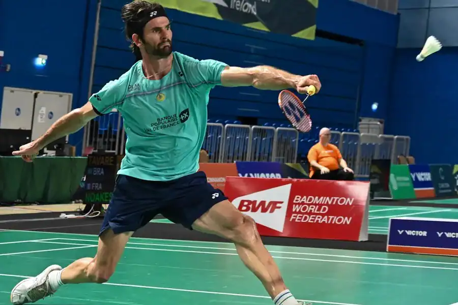 Lucas Mazur en fente pour une frappe lors d'un match de para badminton, devant un panneau Badminton World Federation